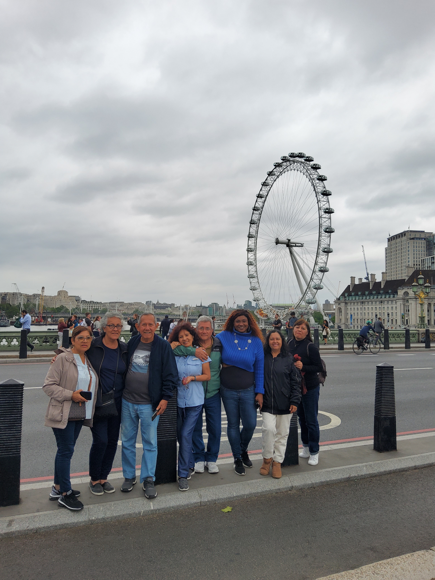 Happy tour group posing in front of London Eye during daytime sightseeing tour